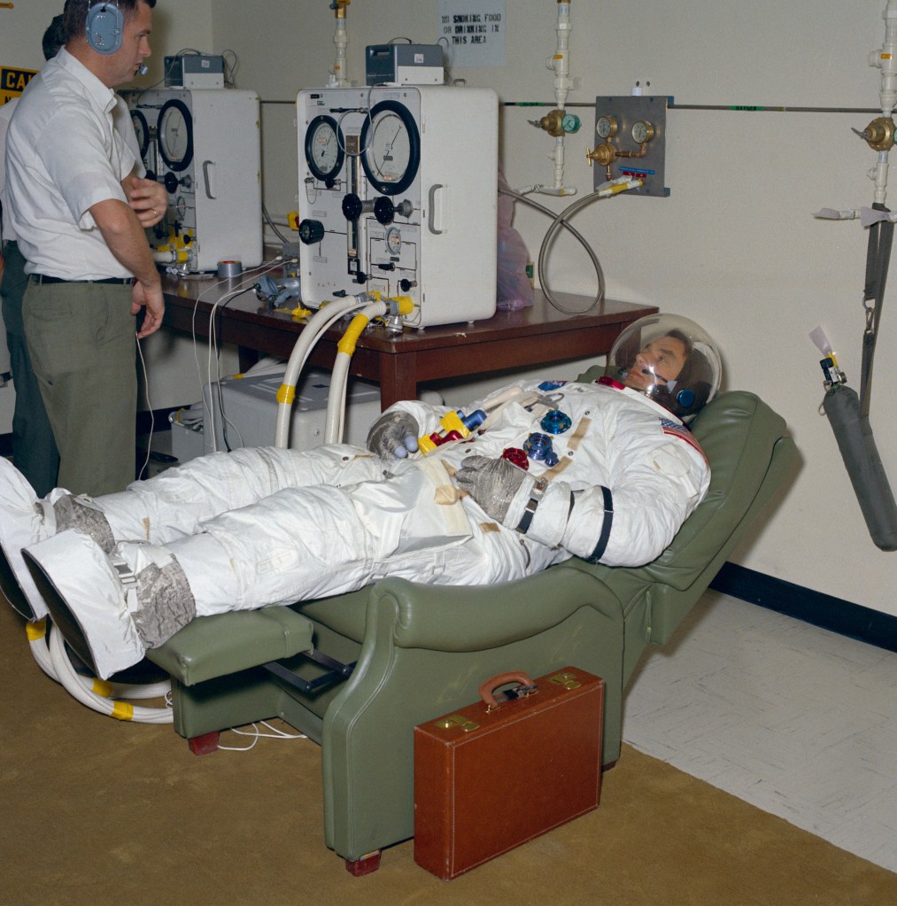 A man clad in a white spacesuit lies supine in a recliner