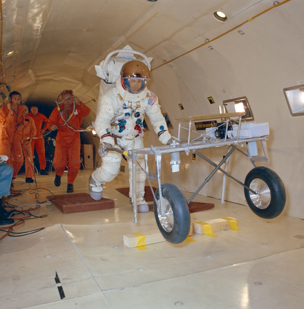 An astronaut wearing a white spacesuit floating in zero-gravity plane testing a golf cart like vehicle