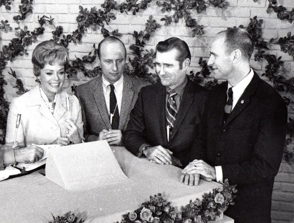 Black and white image of one woman and three men sitting behind a desk.