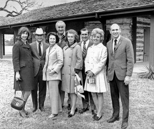 Black and white image of four couples standing in front of a log cabin.