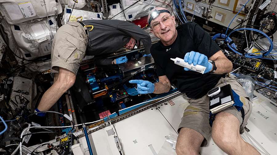 Astronauts (from left) Butch Wilmore and Don Pettit install futuristic exercise gear with advanced bicycling, rowing, and resistive capabilities inside the Columbus laboratory module.