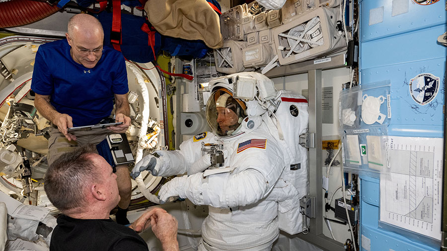 Astronauts Don Pettit (top) and Butch Wilmore (bottom) assist astronaut Nick Hague (center) as he tries on and evaluates his spacesuit in a pressurized configuration inside the Quest airlock.