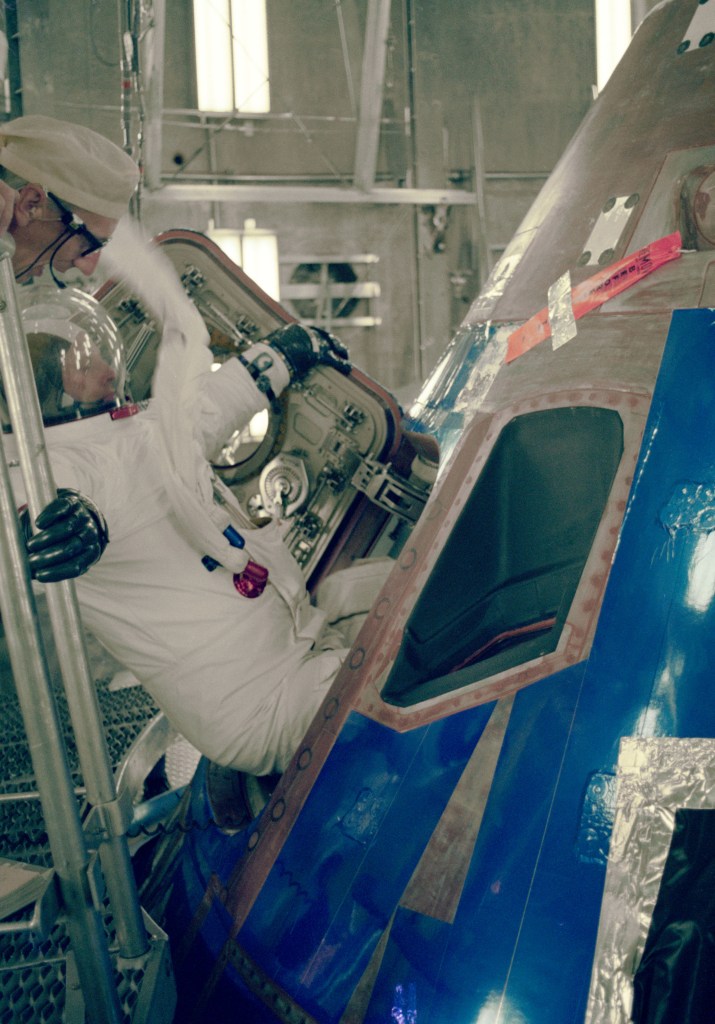 A white suited astronauts entering a blue coated spacecraft