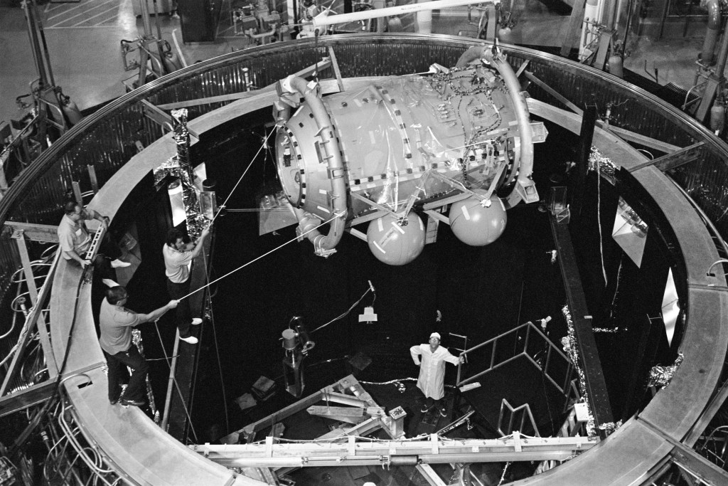 Black and white image of a cylindrical spacecraft being lowered into an altitude chamber