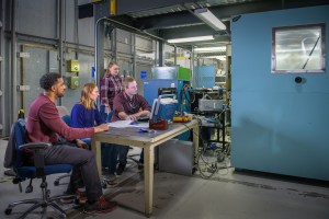 Four researchers gather around a table as they collect data during thermal tests of a cruise motor controller designed for future electrified aircraft propulsion systems. 