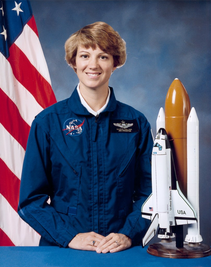 Portrait of a woman wearing a blue jumpsuit with a partially visible US flag in the background