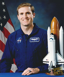 Portrait of a man in a blue jumpsuit with a partially visible US flag in the background