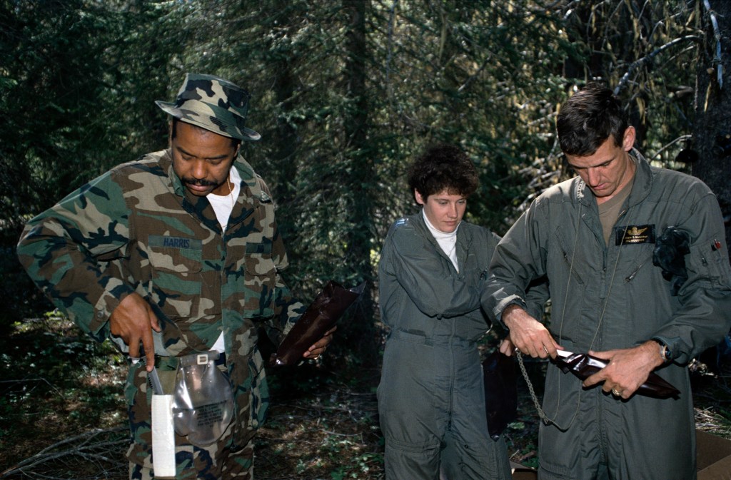 Two men and one woman dressed in either camo or olive drab fatigues in a forest setting