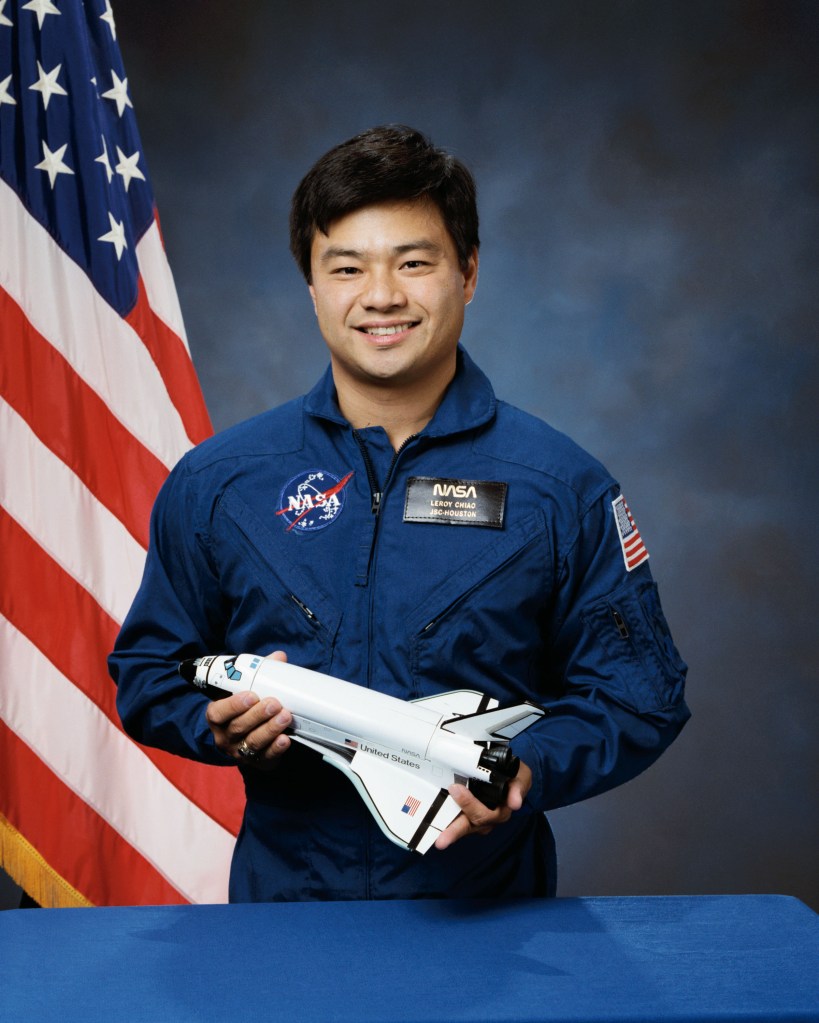 Portrait of a man wearing a blue jump suit with a partially visible US flag in the background