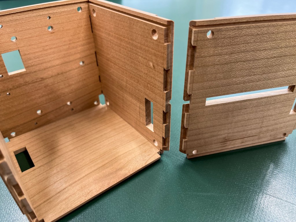 An open box is made of four wooden panels. One additional panel is to the side. The edge of the additional panel matches up with the open box, like a jigsaw puzzle. 