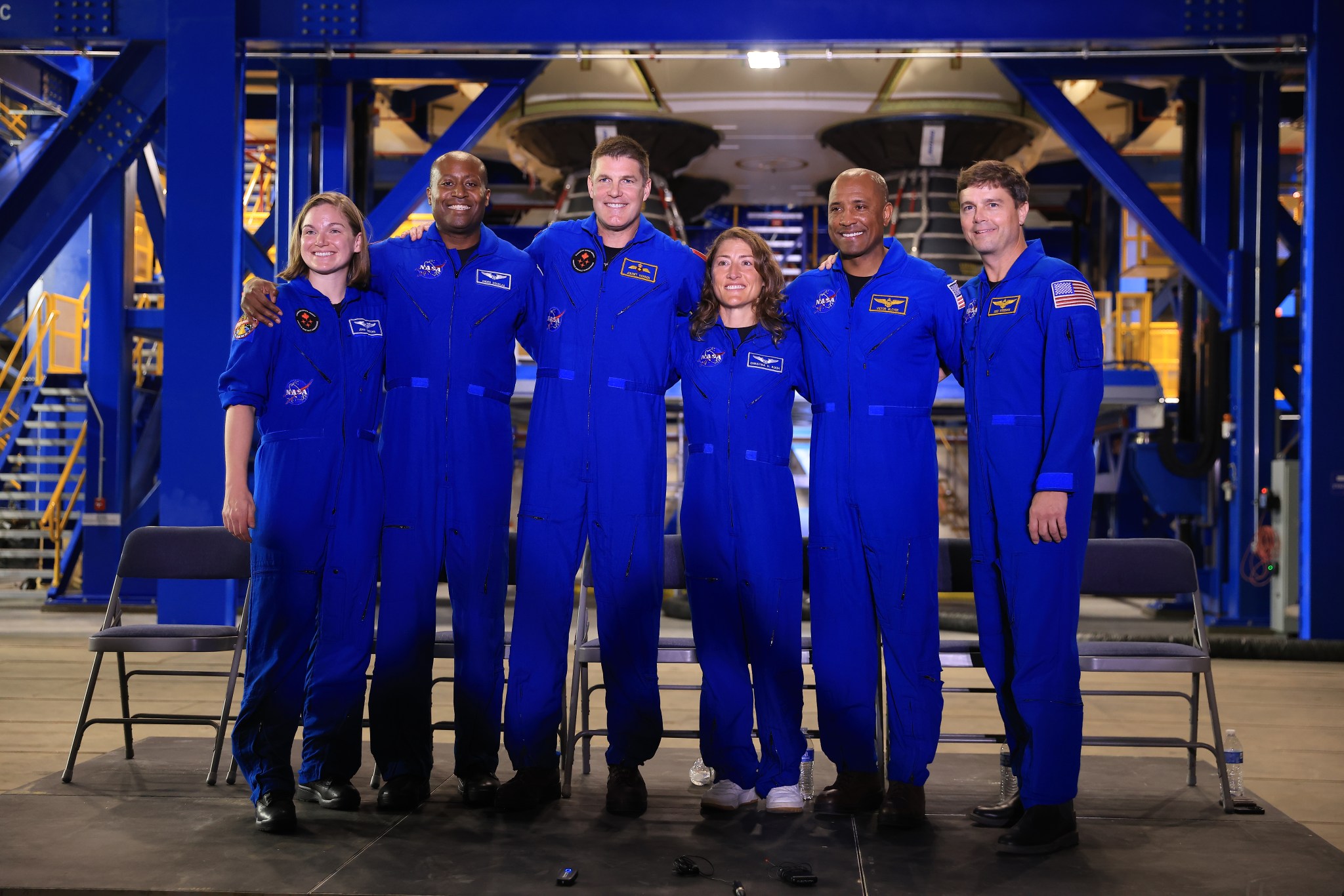 Six astronauts, all in blue jumpsuits, pose together for a photo.