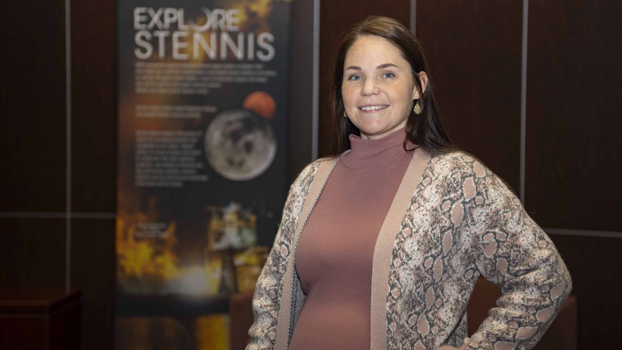 Heather Seagren pauses for a photo in front of an Explore Stennis poster