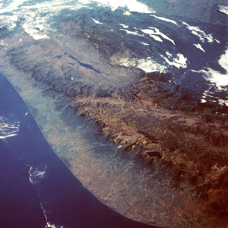 View from the space shuttle of a mountainous coastline and a large body of water in the lower left of the photo.