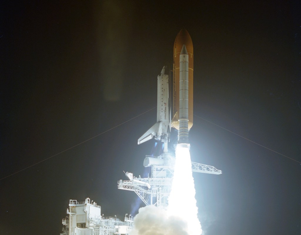 Image of a space shuttle taking off on a pillar of flame at night.