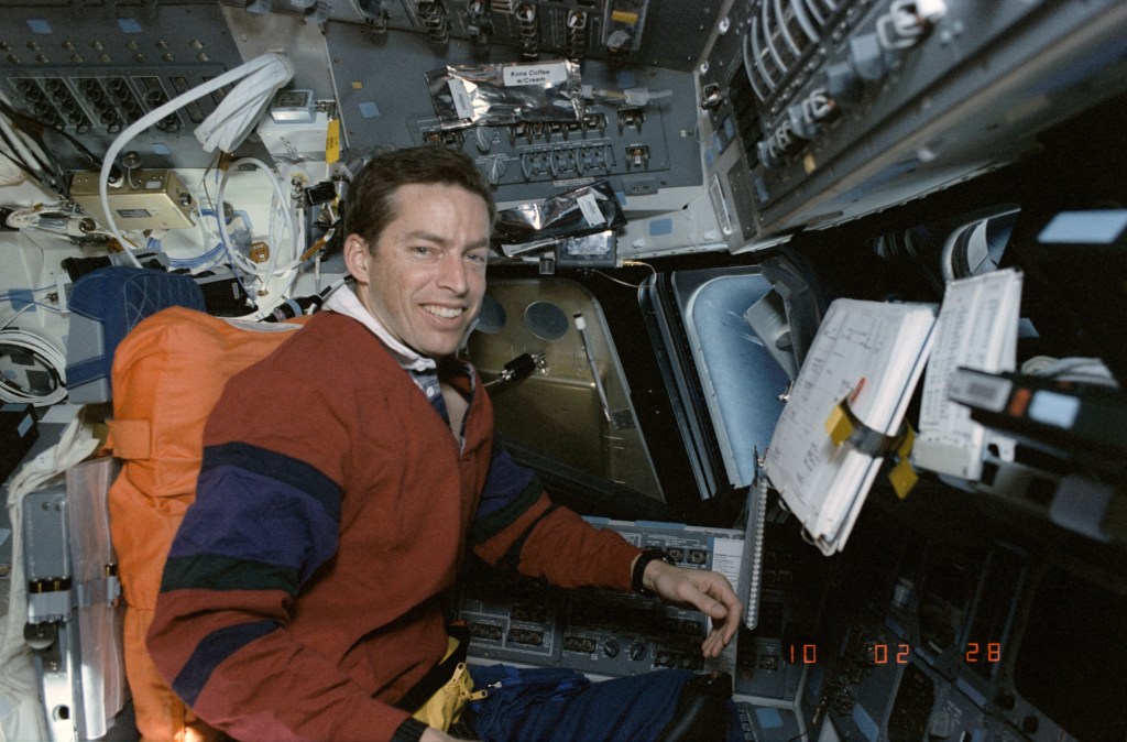 View of a male astronaut sitting in the commander's seat of the space shuttle in orbit.