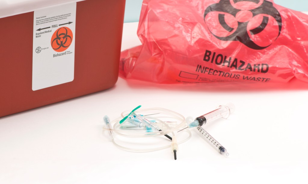 Used medical equipment with biohazard bag and sharps container.