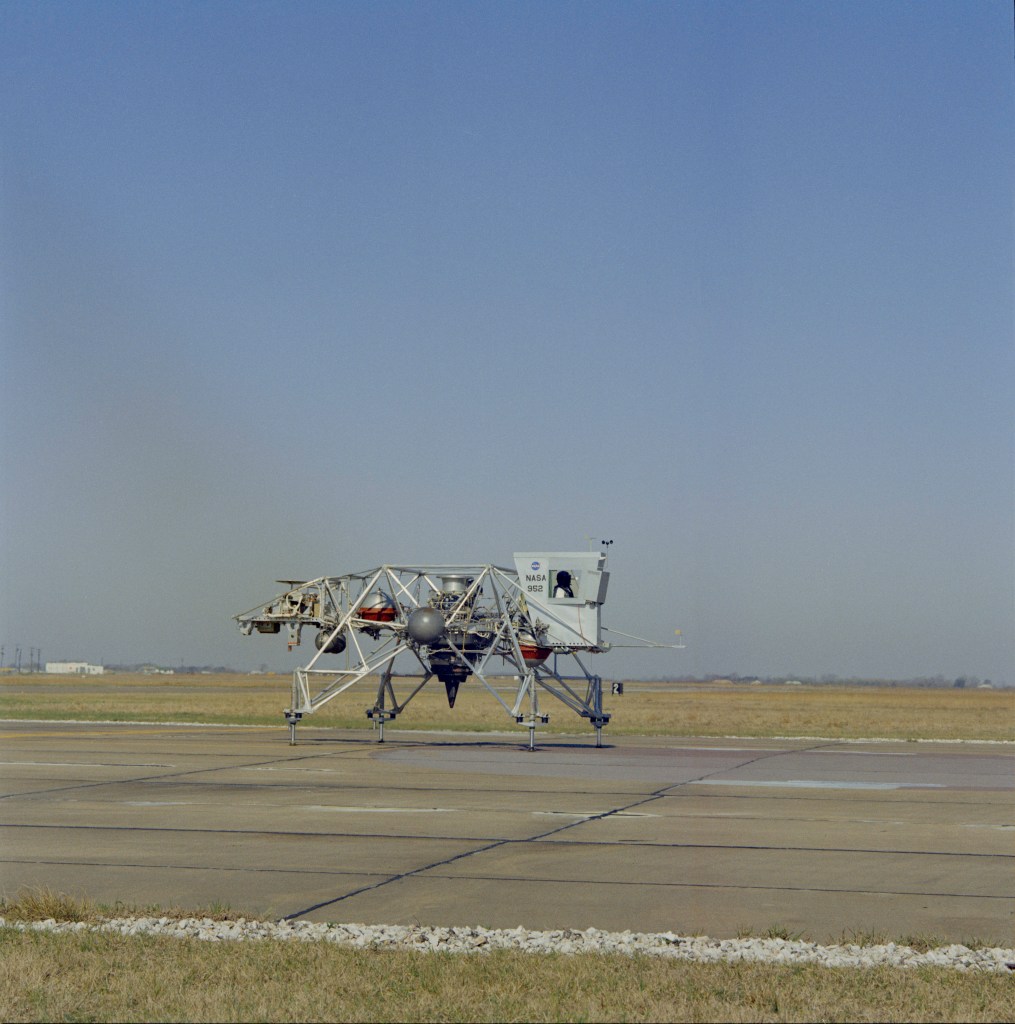 Image of four-legged metal contraption, the Lunar Landing Training Vehicle, sitting on a runway, against the background of a blue sky.