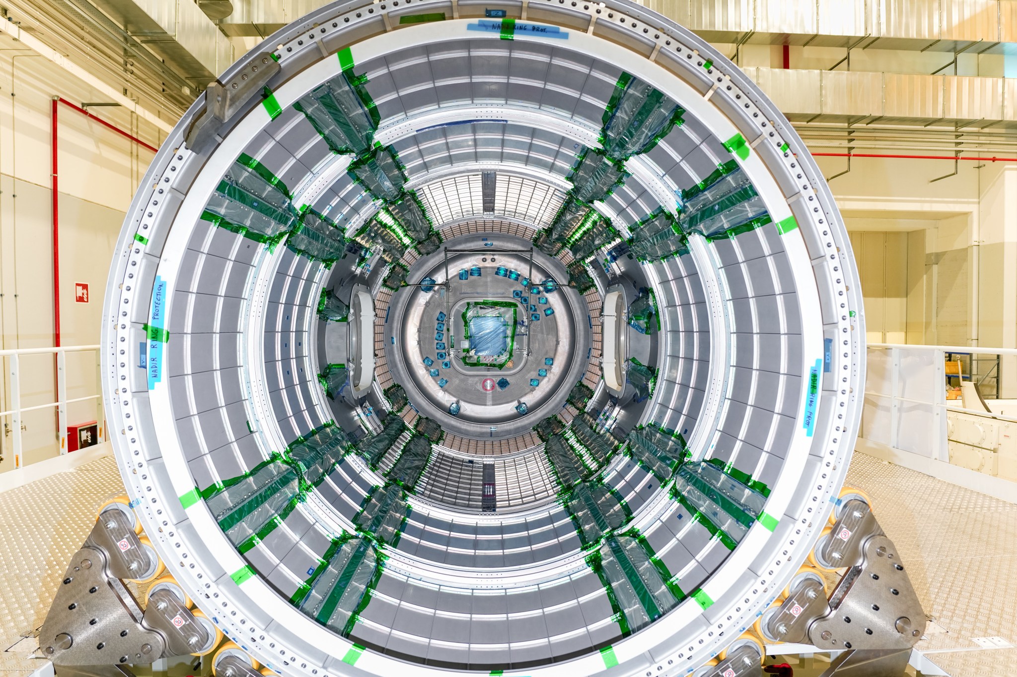 nterior view of Gateway’s Habitation and Logistics Outpost (HALO) in the cleanroom at Thales Alenia Space in Turin, Italy. The cylindrical module features metallic panels and green-wrapped components along its interior.