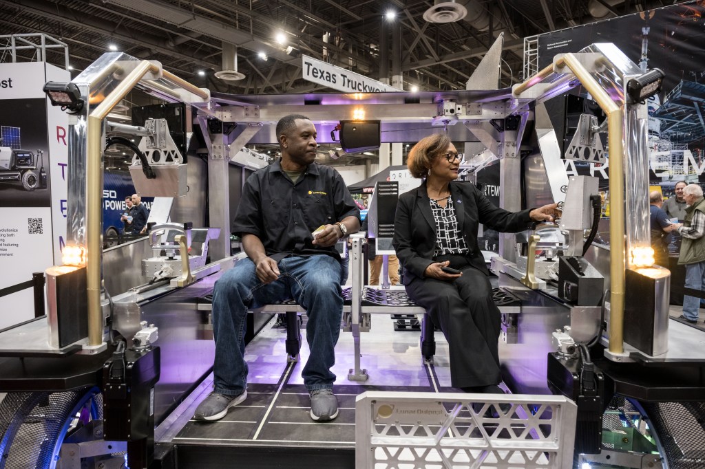 Three individuals interacting around a lunar rover by Intuitive Machines at an exhibit.