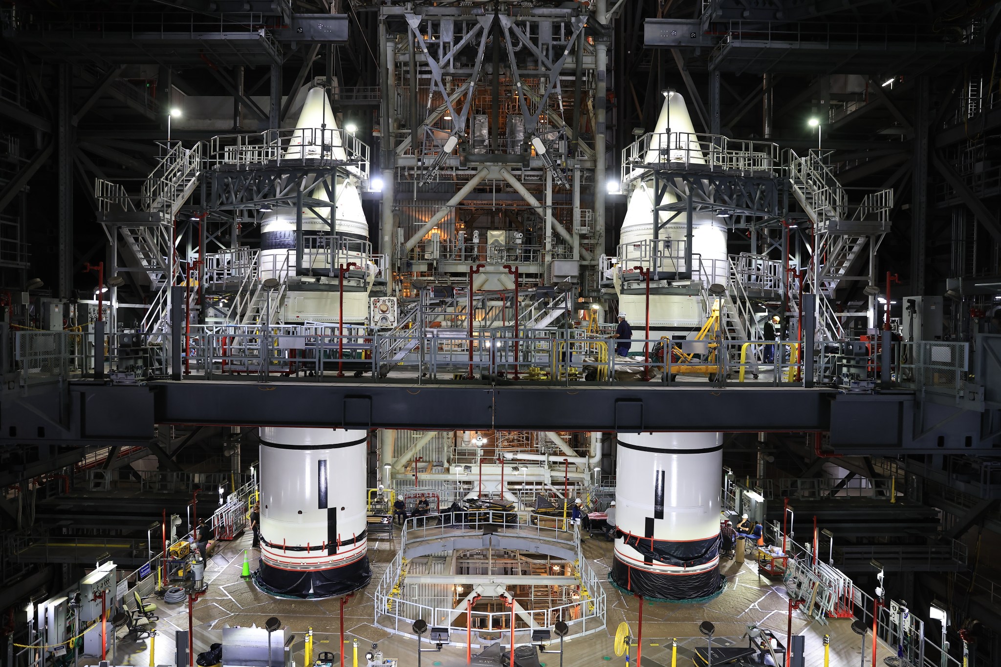 Two massive white rocket boosters stand inside the Vehicle Assembly Building. There are balconies and stairs around the boosters, reaching all the way up to the recently integrated nose cones.