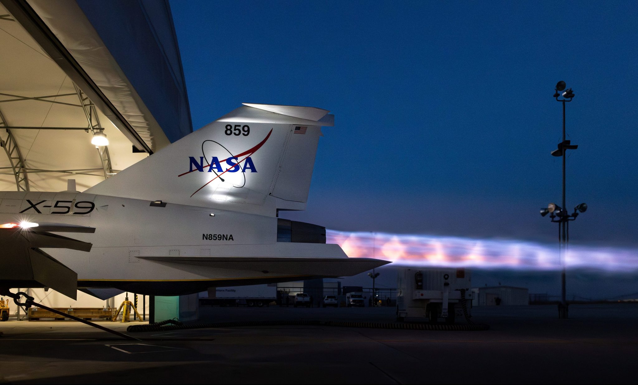 NASA's supersonic X-59 undergoes maximum afterburner testing at dusk, with a bright, fiery exhaust extending from its tail. Visible in the superhot plume, which features vibrant hues of blue, purple, and orange, are distinct Mach diamonds—also known as shock diamonds.