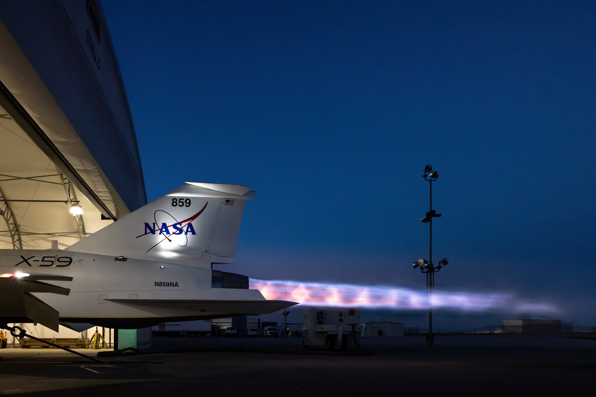 NASA's supersonic X-59 undergoes maximum afterburner testing at dusk, with a bright, fiery exhaust extending from its tail. Visible in the superhot plume, which features vibrant hues of blue, purple, and orange, are distinct Mach diamonds—also known as shock diamonds.