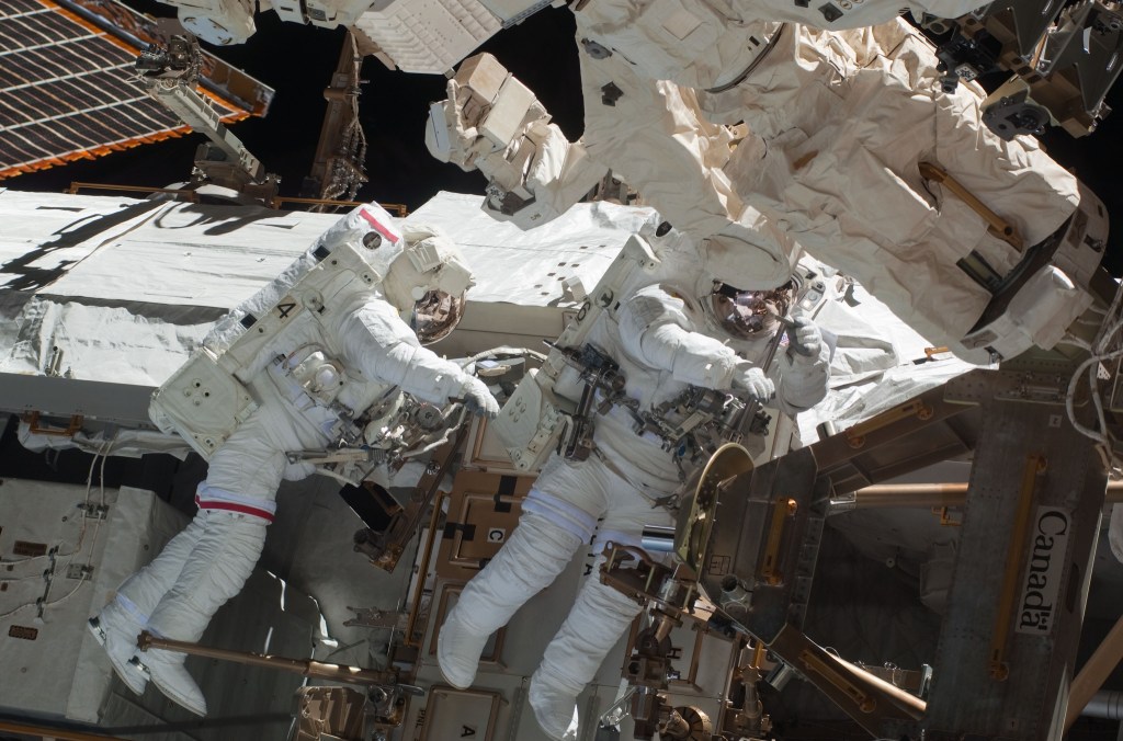 Image of two astronauts wearing white spacesuits during a spacewalk outside the International Space Station.