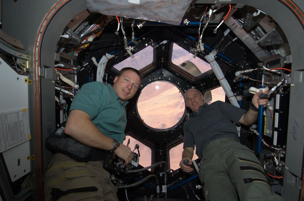 Two male astronauts are seen inside the space station's cupola with the Earth visible through its windows.