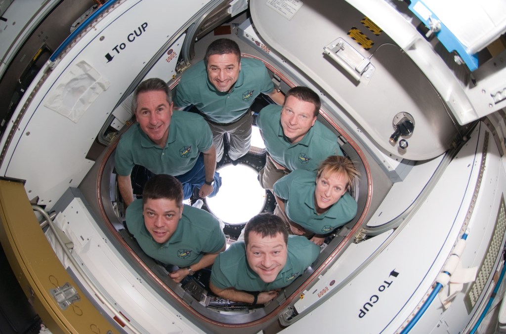 Image of six astronauts wearing green T-shirts inside the space station's cupola.