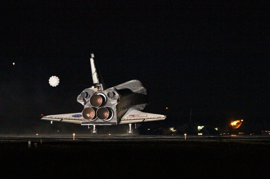 View of a space shuttle making a night landing, with its drogue parachute just deploying.