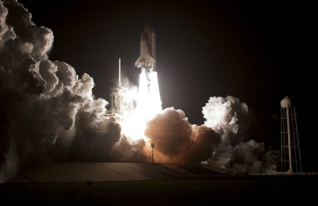 Nighttime image of a space shuttle lifting off on a pillar of fire.