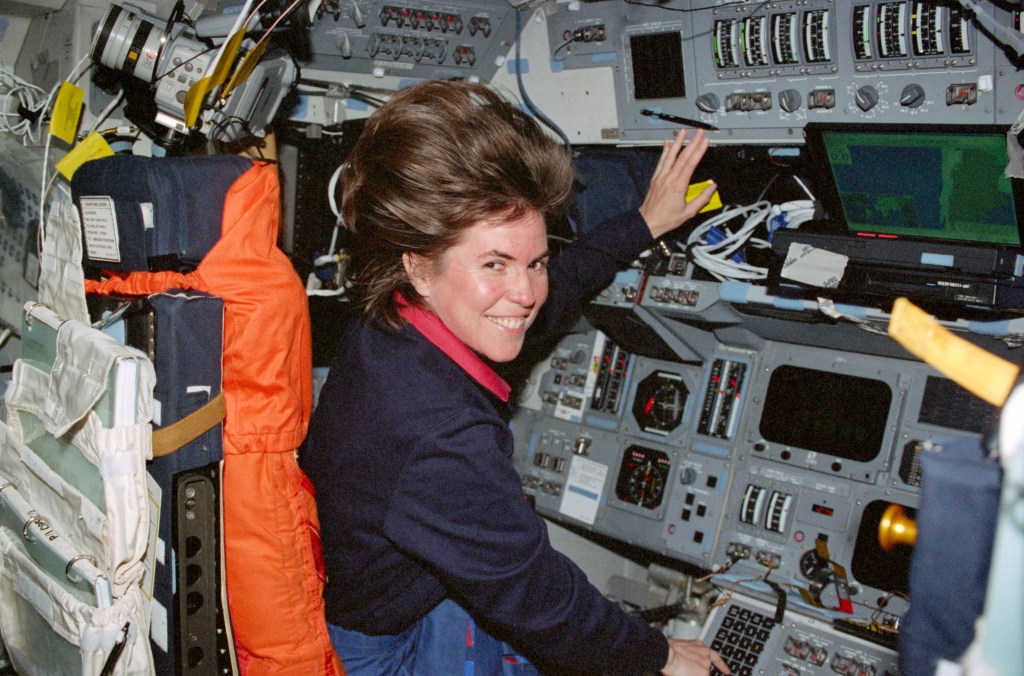 Image of a female astronaut floating in the commander's seat on the shuttle's flight deck.