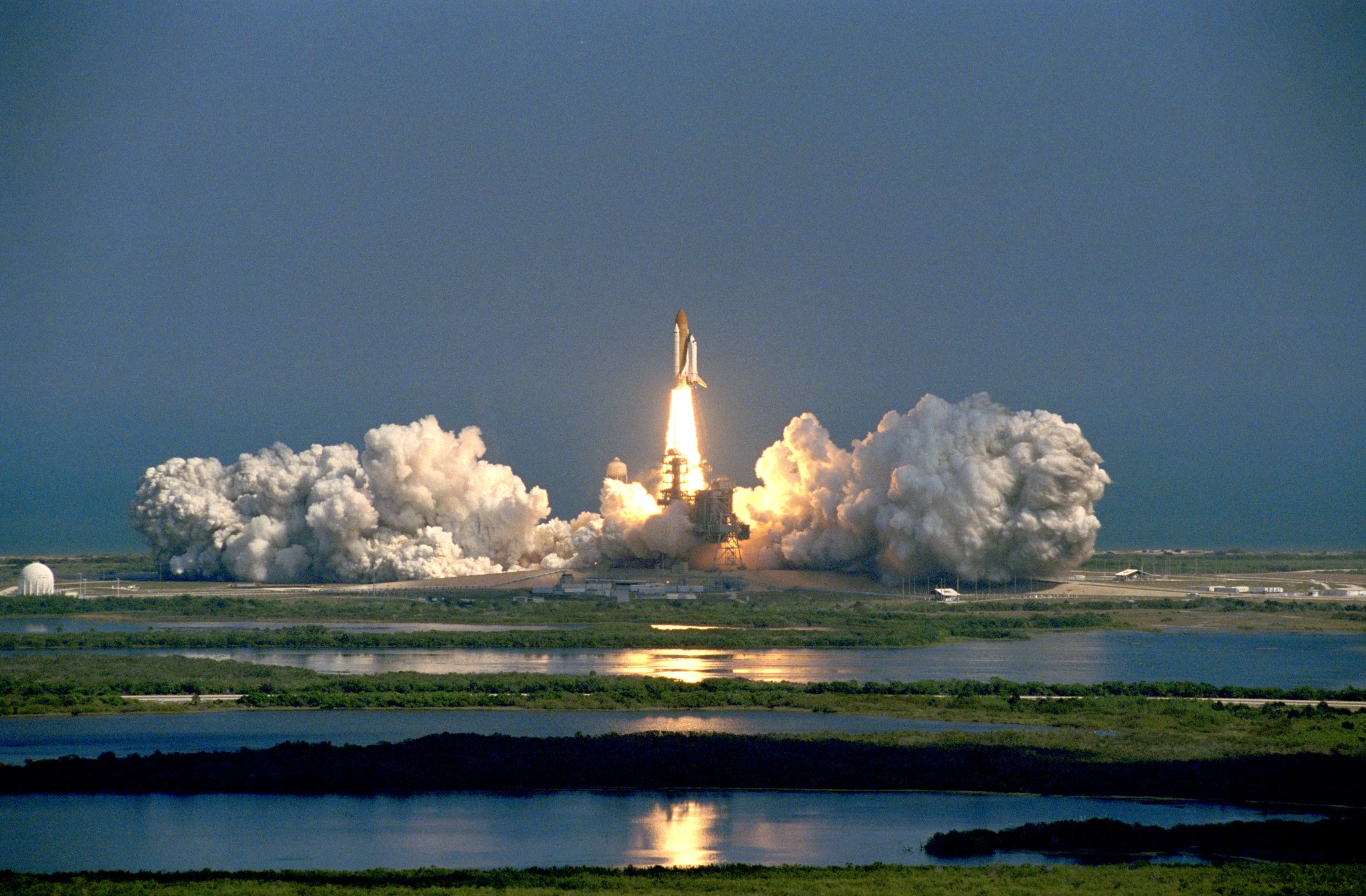 Image of a space shuttle lifting off on a pillar of fire into a blue sky.