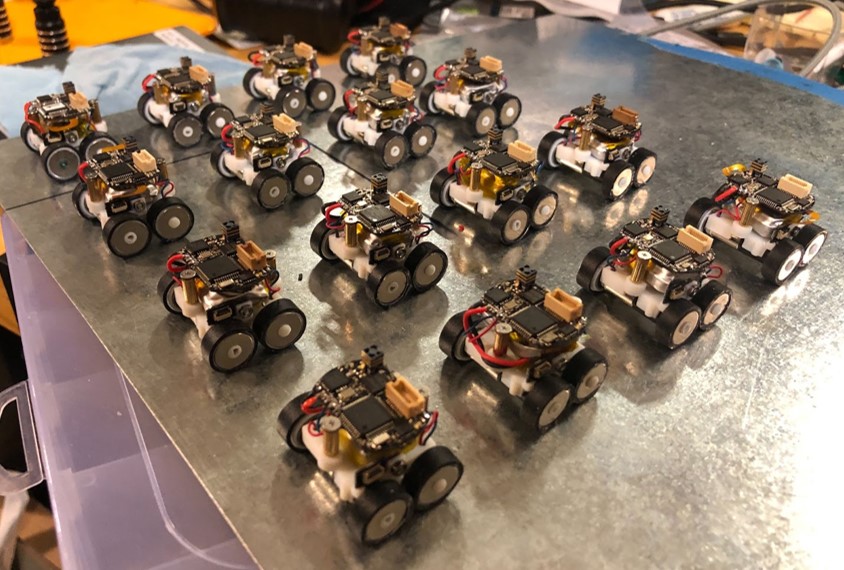 A fleet of tiny robotic rovers sit in rows on a tabletop.