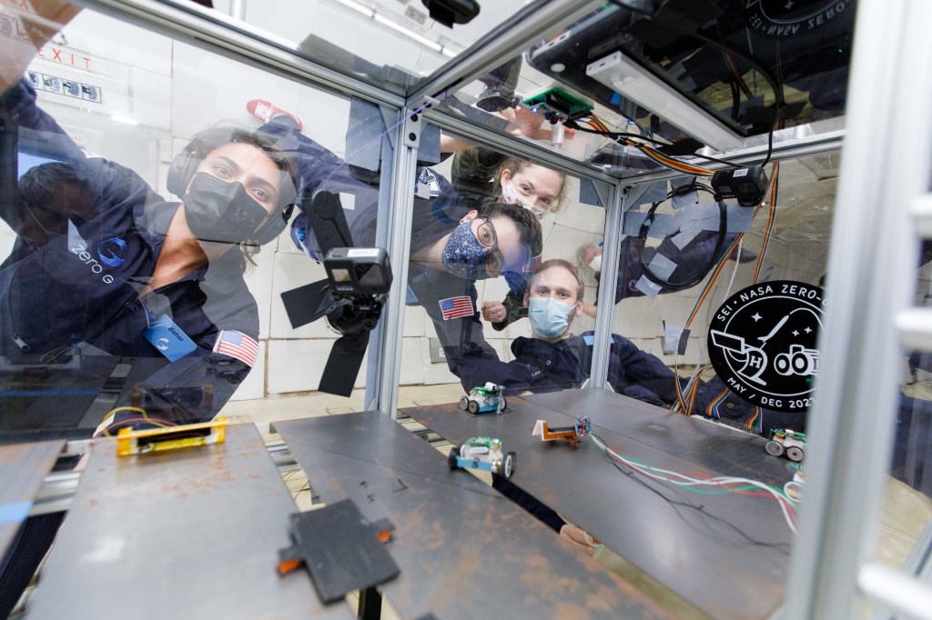 Four researchers on a parabolic flight peer into a clear container at their experiment. Flight-Tested Technologies for Safety in Space Head to the Moon