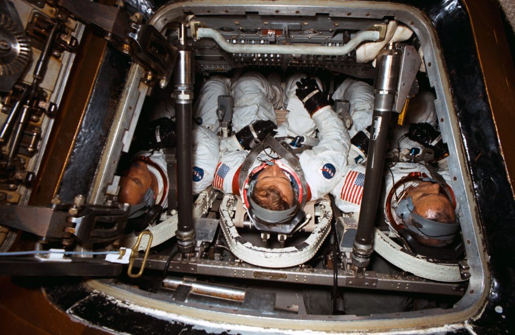 Image of three astronauts in white space suits inside their spacecraft seen through the open hatch.