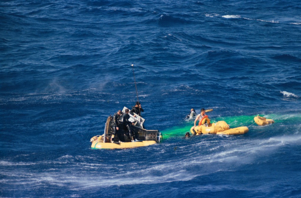 Image of a space capsule floating in the ocean, with a life raft nearby.