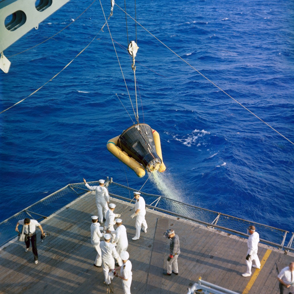 Image of sailors hoisting a space capsule onto the deck of an aircraft carrier.