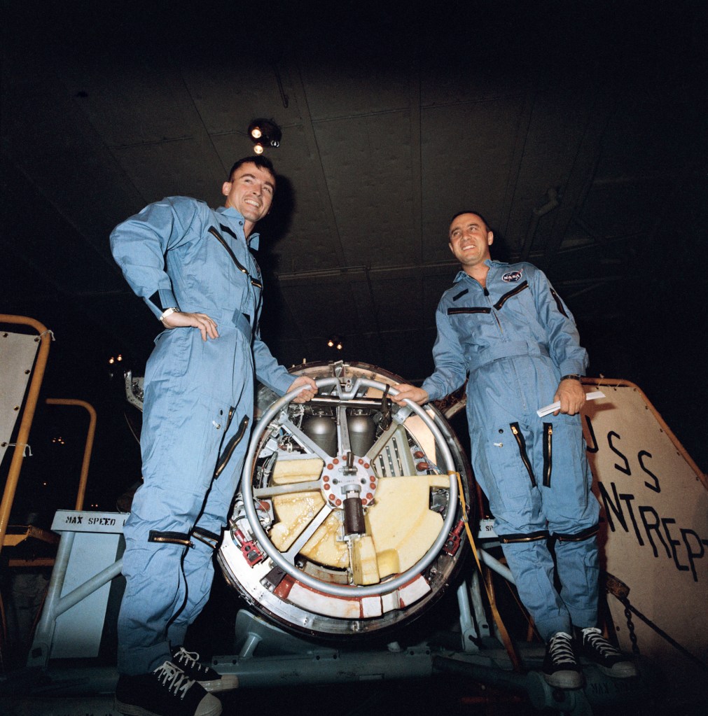 Two astronauts wearing blue flight suits pose with their space capsule aboard the recovery ship.