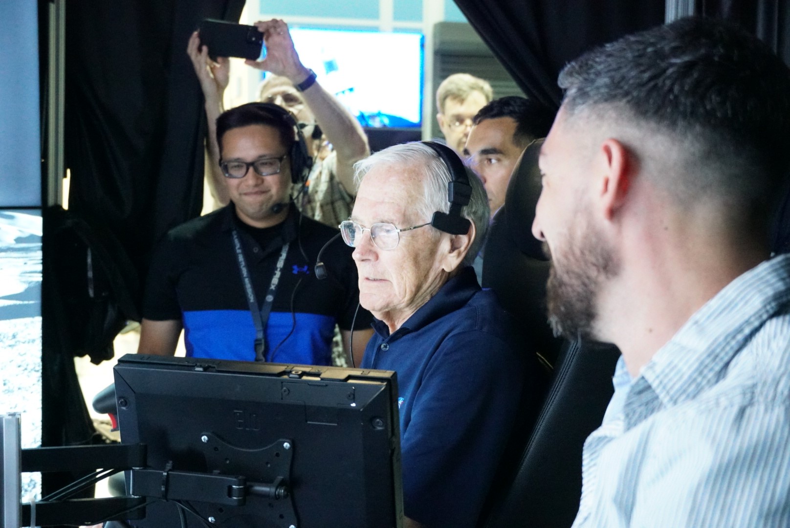 NASA employees and retired NASA astronaut Charlie Duke gather around a computer screen for a lunar rover simulation.