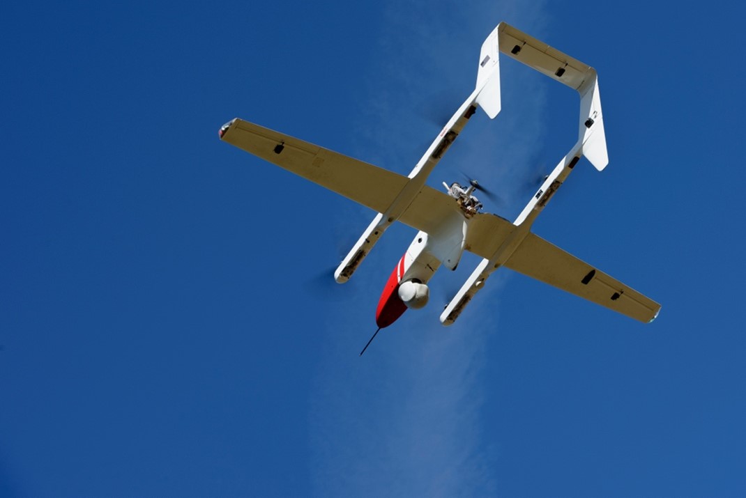 Looking up, the underside of a small white aircraft is shown flying against a blue sky.