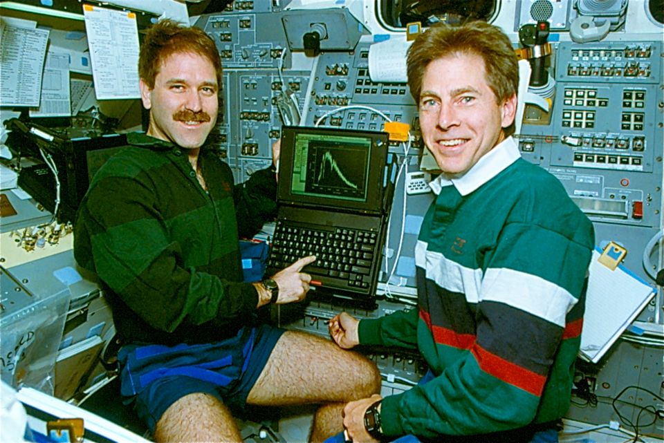 View of two male astronauts with a laptop working in the shuttle's aft flight deck.