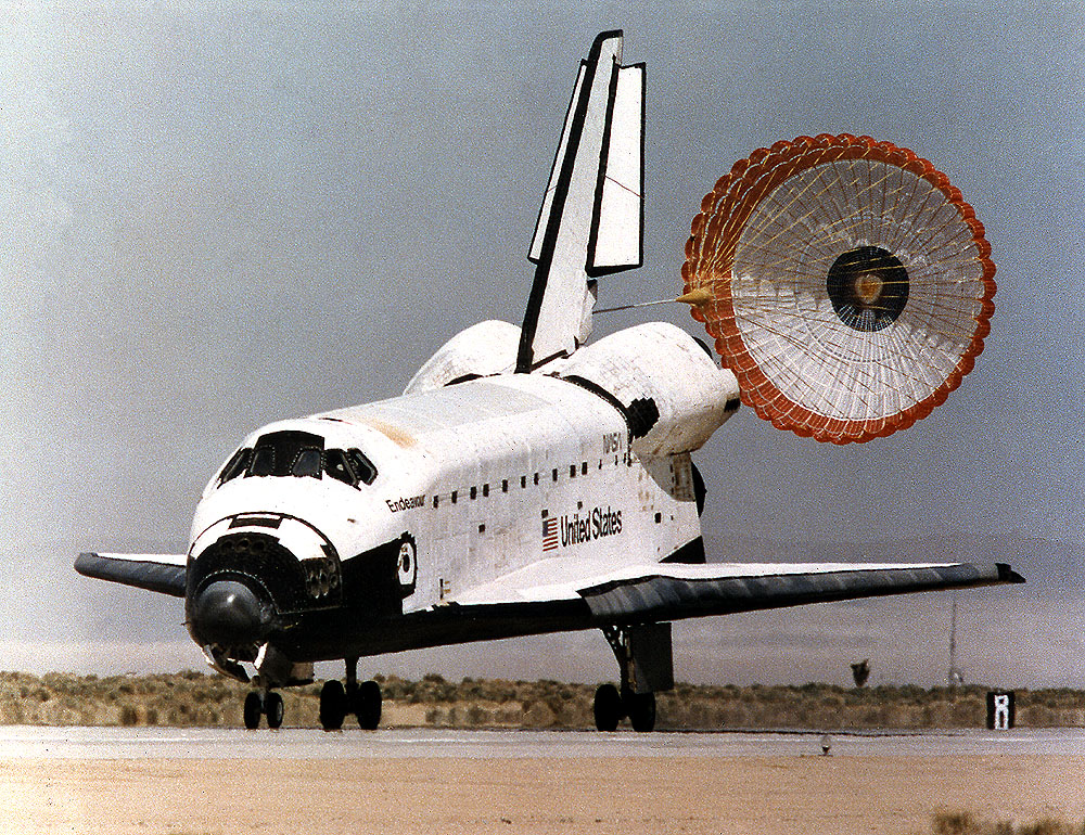 Photograph of a space shuttle landing on a desert runway with the drag chute open.