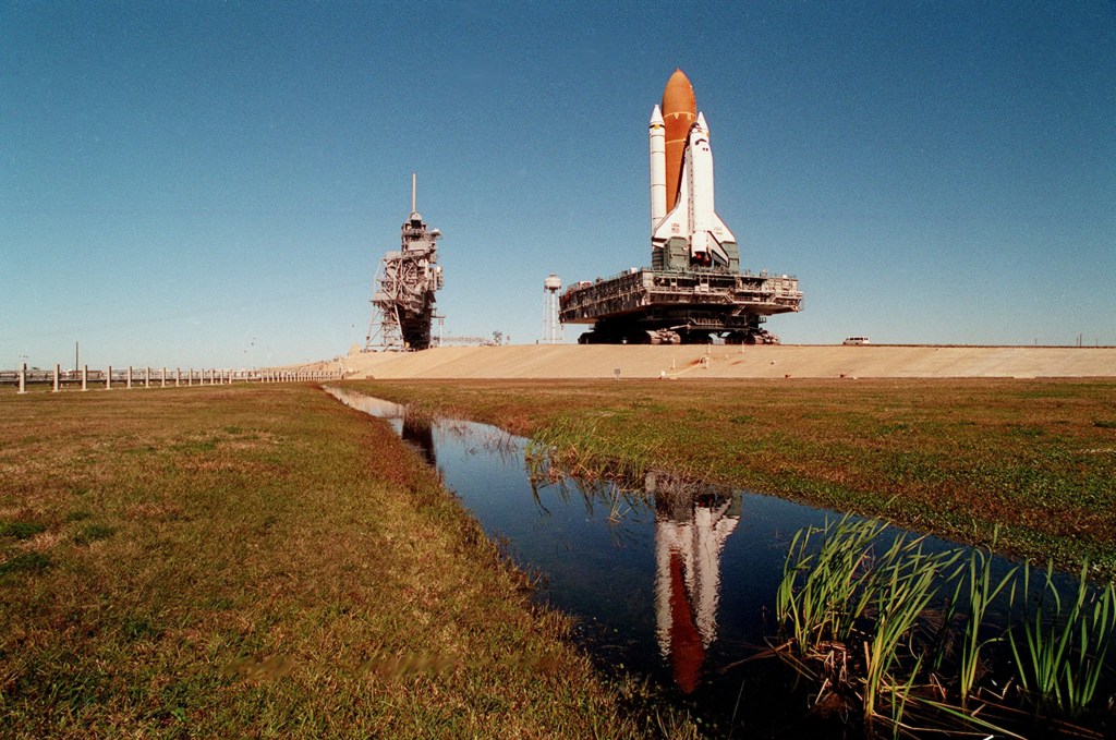 Daytime view of a space shuttle approaching its launch pad during rollout.