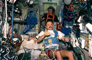 Astronaut Shannon Lucid (background) exercises on the treadmill in the Mir space station Base Block while Mir-21 flight engineer Yury Usachev is wired for an experiment. 