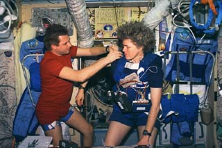 Mir-21 commander Yuri Onufriyenko (left) adjusts the harness used in the Anticipatory Posture Experiment on Astronaut Shannon Lucid. The experiment is being performed in the Mir space station Base Block. 