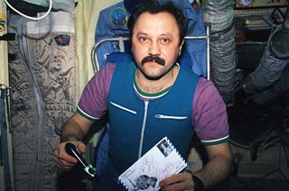 Mir-21 Flight Engineer Yury Usachev holds a peeler and a piece of mail received along with some food. 