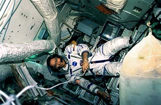 John E. Blaha, in a Russian EVA suit, in a Mir module surrounded by floating items. 
