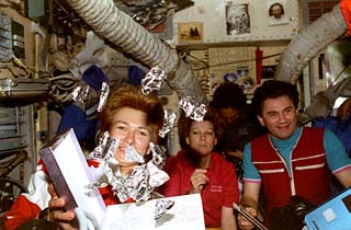 Chocolate candy shuttles fly freely about the Mir during the gift exchange. Elena Kondakova (front), Eileen Collins (center), and Vasily Tsibliev (right) join in the exchange.