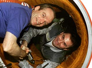Charlie Precourt and Vasily Tsibliyev shake hands in the open hatch between the Mir Space Station Docking Module and the shuttle. 